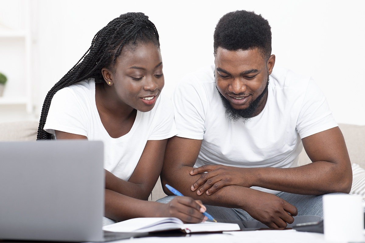 Young black couple planning budget together at home and writing notes